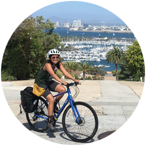 Jacq Le riding a bike with a view of downtown San Diego behind her