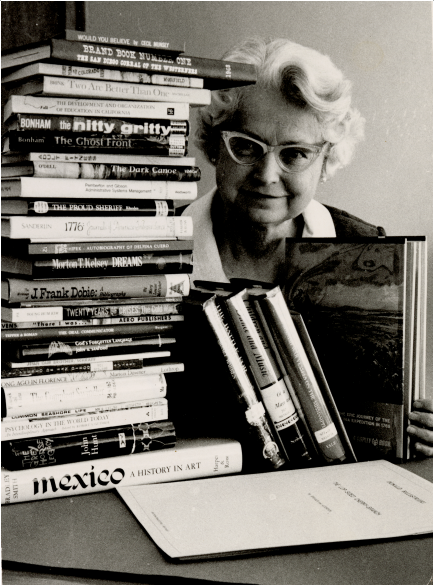 Black and white photo of Clara Breed with stack of books