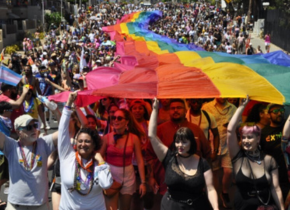 Photograph of the San Diego Pride Parade featuring a street full of people holding up an extremely long rainbow flag