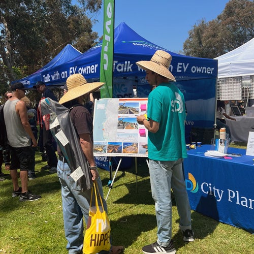 A City staffmember speaking to a visitor at an electric vehicle booth