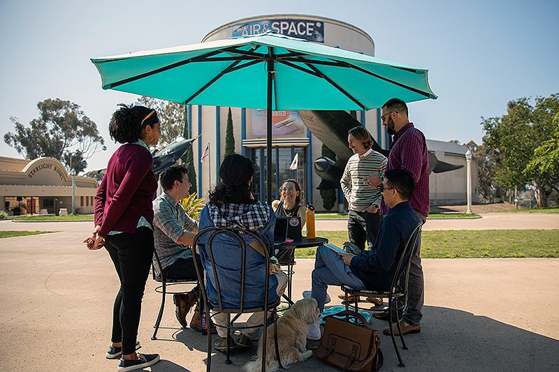 Performance and Analytics staff discussing a project at a table in front of the Air and Space Museum in Balboa Park.