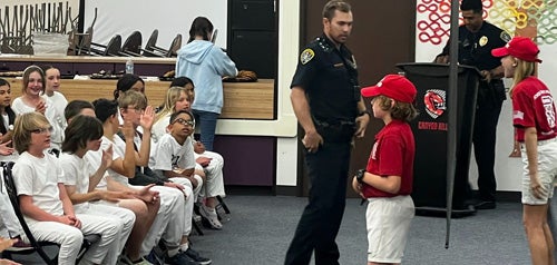 A school safety patrol member speaking other schoolmates about the program with the assistance of a police officer