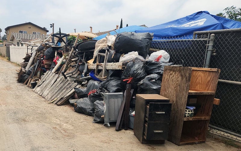 Illegally dumped trash piled against a chain link fence