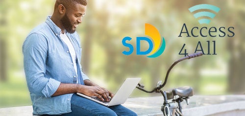 Smiling man working on a laptop in a park