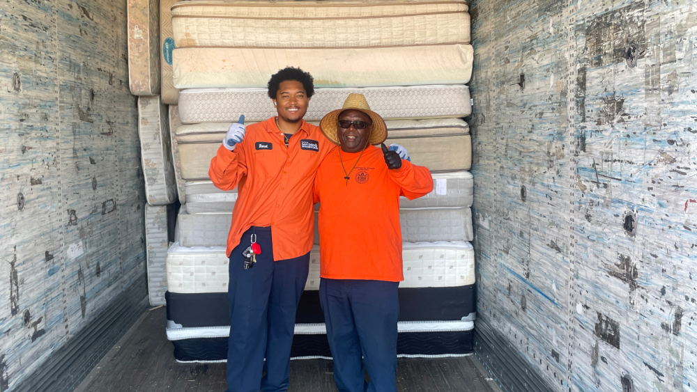 two workers wearing orange with unwanted mattresses behind them ready to be recycled