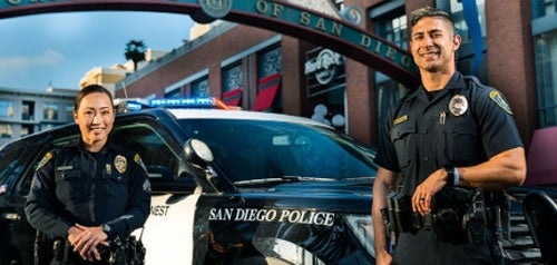 Smiling police officers posing in front of a police car