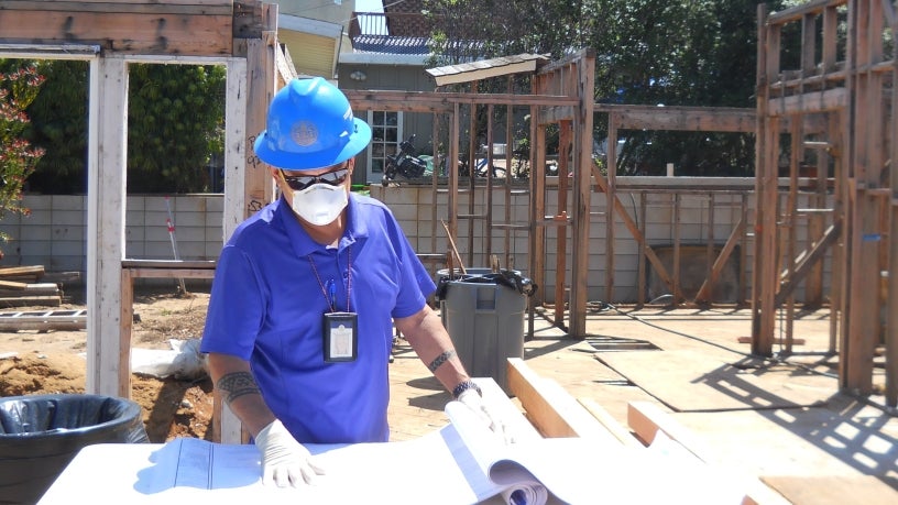 A City inspector uses proper PPE to inspect plans at a construction site. 