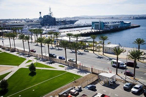 A bayside street lined with palm trees with a docked Navy vessel in the background