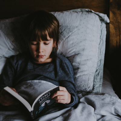 A kid in bed reading a book