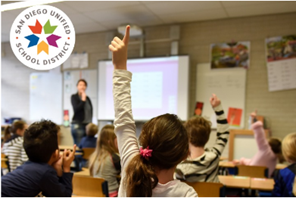 students raising their hands during class, photographed from the back of the class