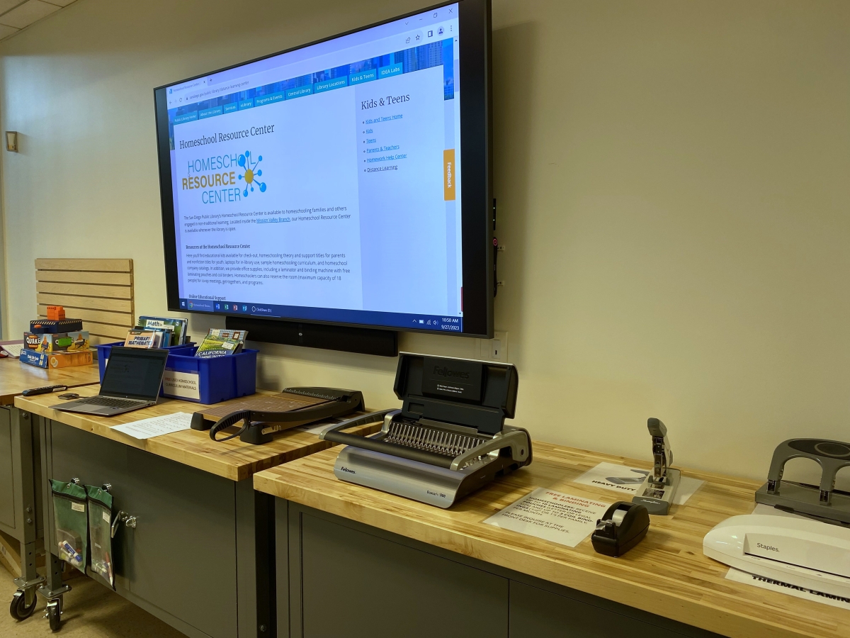 Large monitor on wall; in front are desks with various materials.