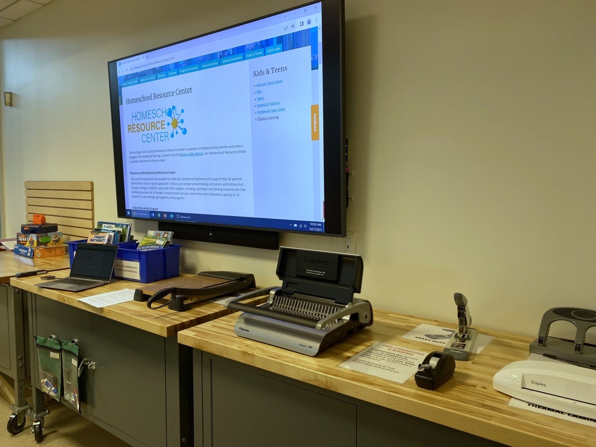 Large monitor on wall; in front are desks with various materials.