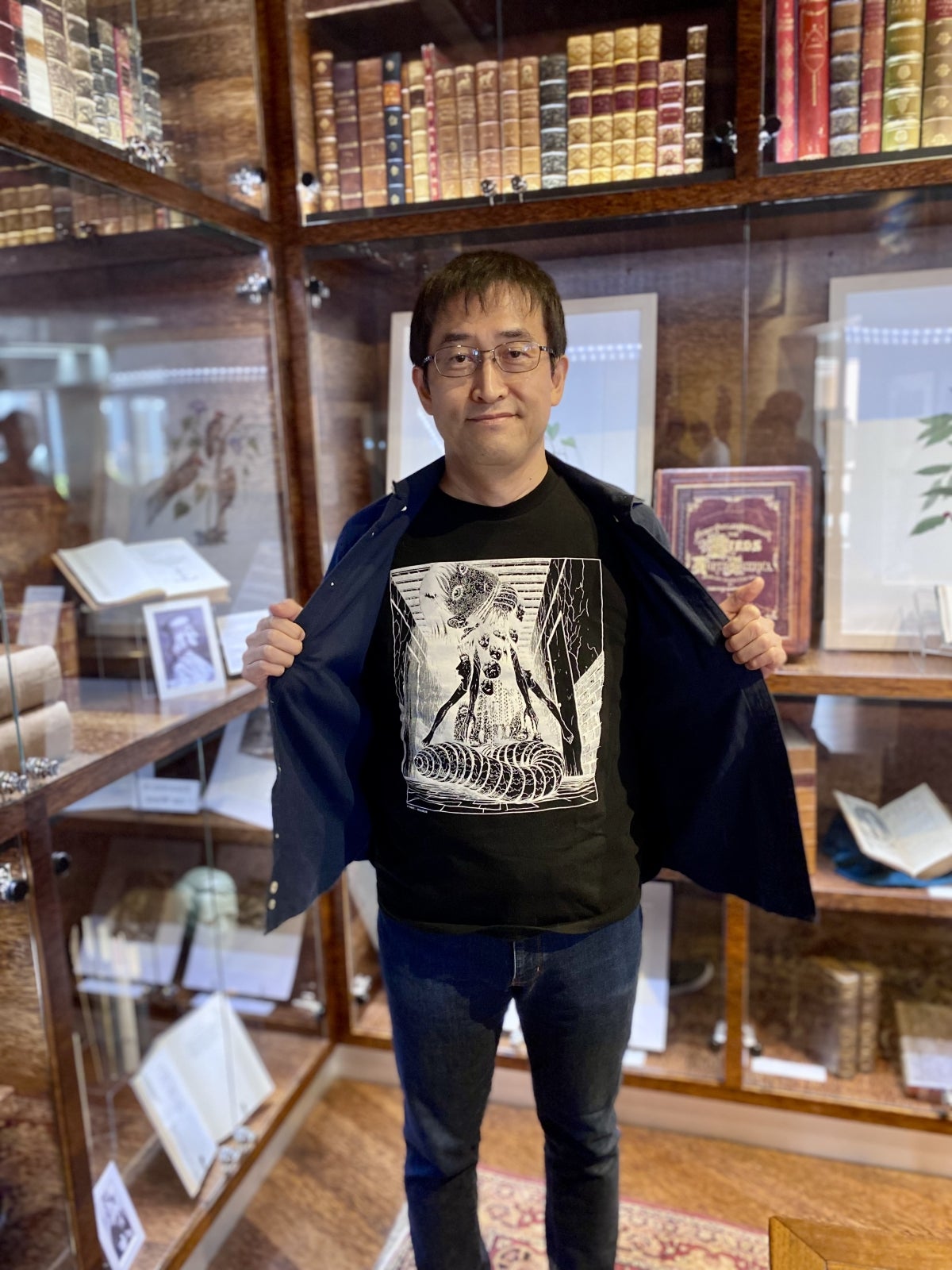 Junji Ito holding his jacket open to reveal the artwork on his shirt