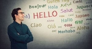 A person with glasses standing in front of a wall with the word hello written in many languages on it.