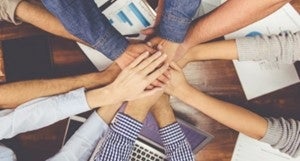 a group of people with placing their hands on top of each other over work documents