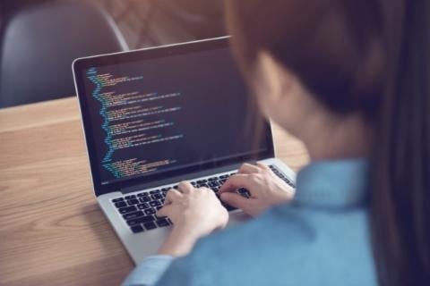 Dark haired student with ponytail working on a computer programming project on their laptop.