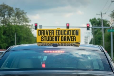 Top of car show sign "Driver Education Student Driver" and stopped at a redlight