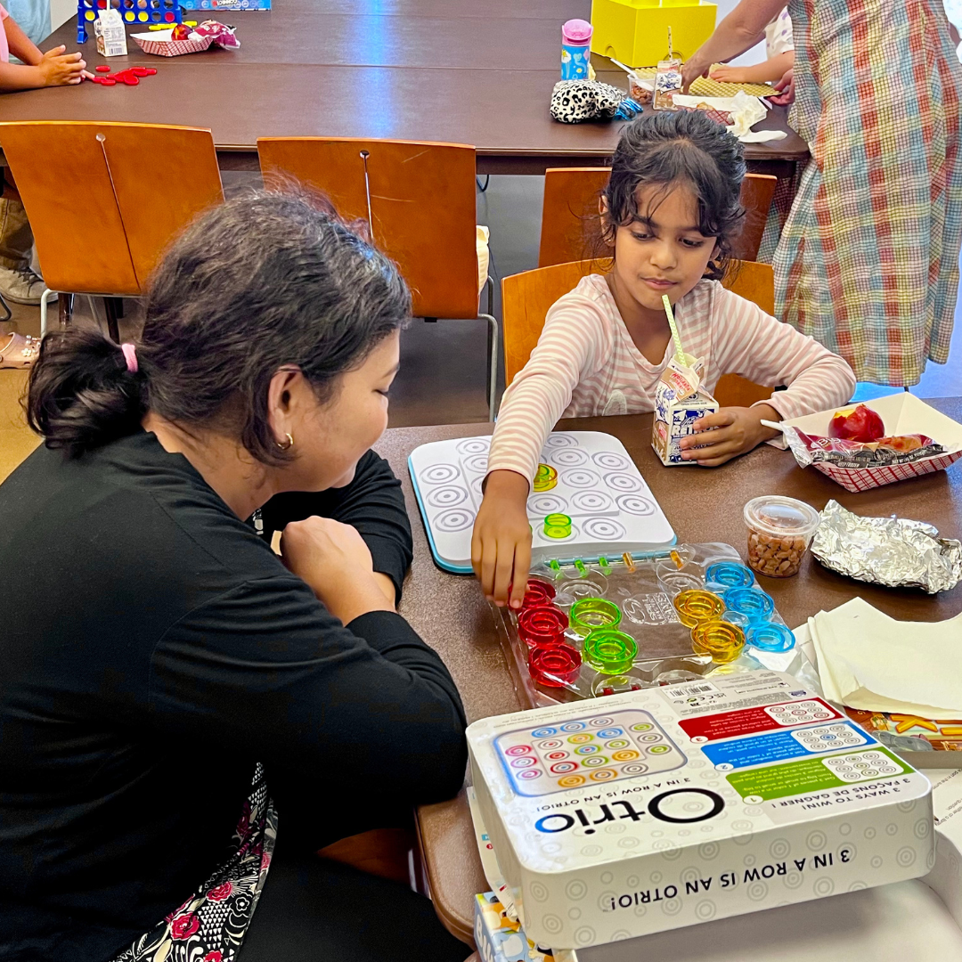 a parent and child are enjoying a fun board game during the summer lunch program.
