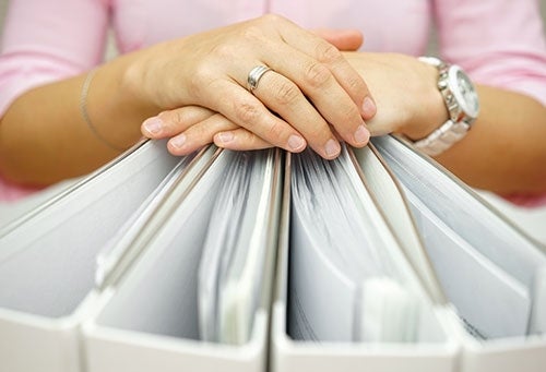 Photo of Hands Folded over a Row of Binders