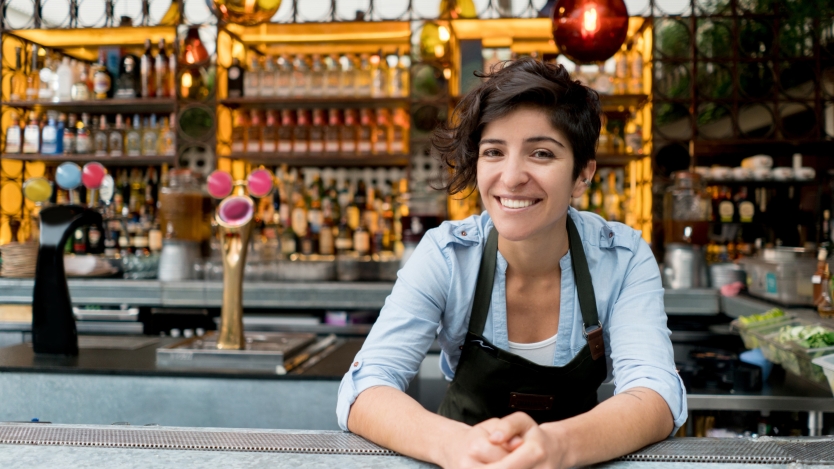 service worker in front of a bar, smiling leaning on the counter