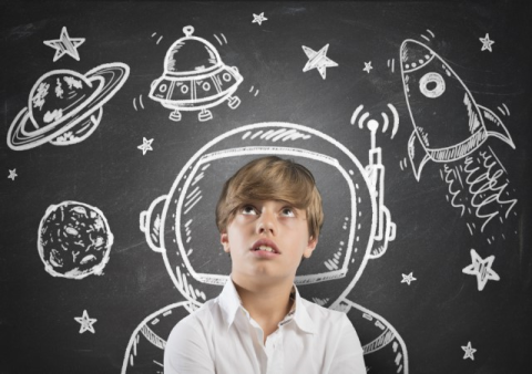 Boy in front of chalkboard with planets and rockets drawn on it